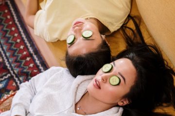 Two women enjoying a relaxing spa day with cucumber masks in a cozy home setting.