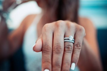 Close-up shot of a woman's hand displaying her engagement and wedding rings with manicured nails.