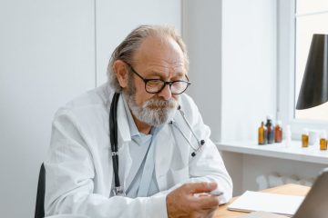 Elderly doctor using laptop for a virtual consultation in a modern office.